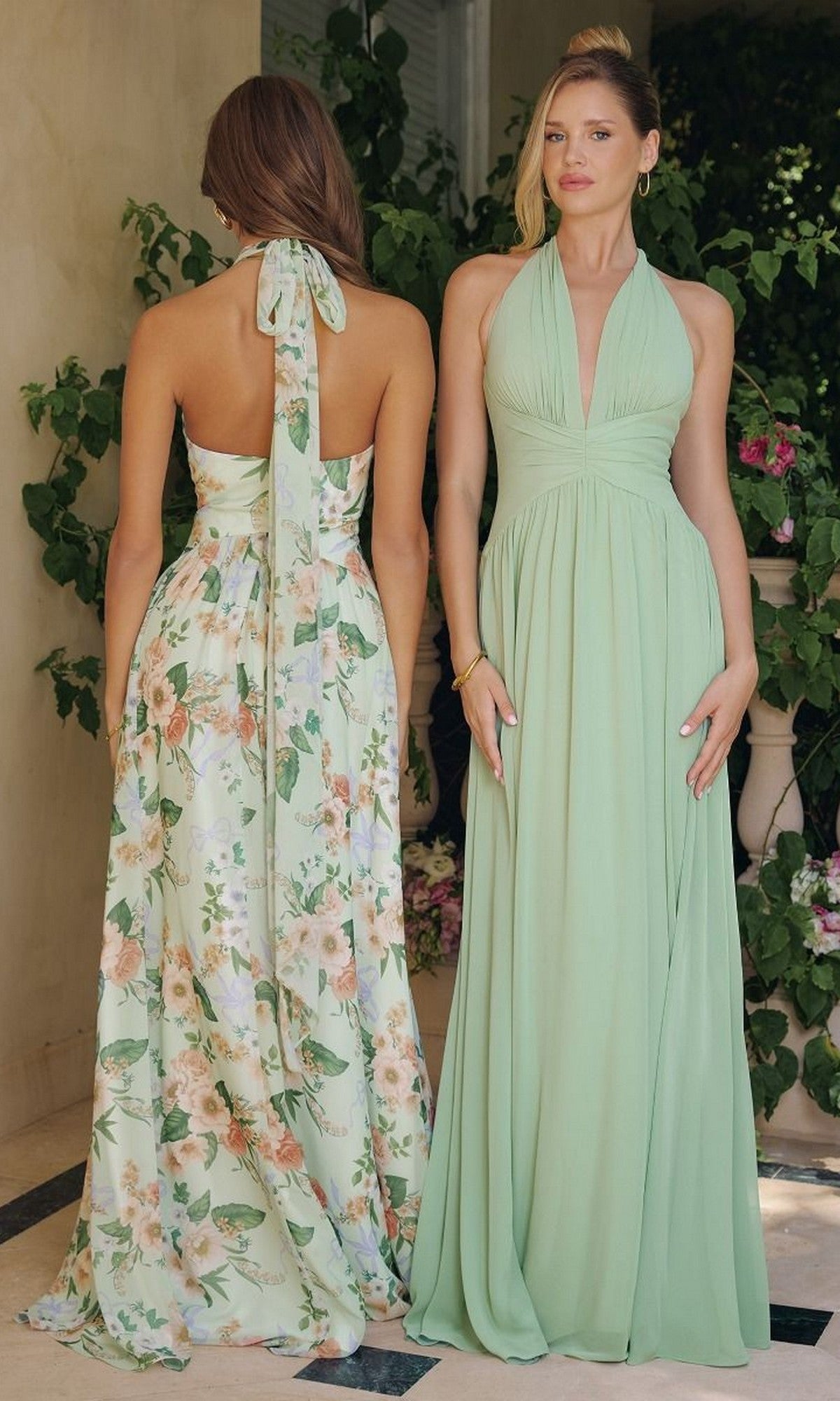 Two women stand before leafy plants—one wears a sage formal open-back dress, the other the Sage Floral Print Long Halter Prom Dress: Amoris T719.